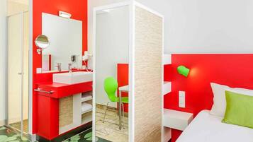 A hotel room with a red and white color scheme, a separate bathroom, a green chair, and a bed with a green pillow.