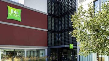 A modern building with a prominent 'ibis Styles' sign, large windows, and a well-maintained outdoor area with plants.