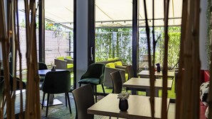 Un espace intérieur aménagé avec des tables et des chaises, de grandes fenêtres et une vue sur la terrasse extérieure.