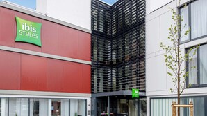 Un bâtiment moderne avec une façade rouge et une enseigne verte sur laquelle on peut lire « ibis Styles ».