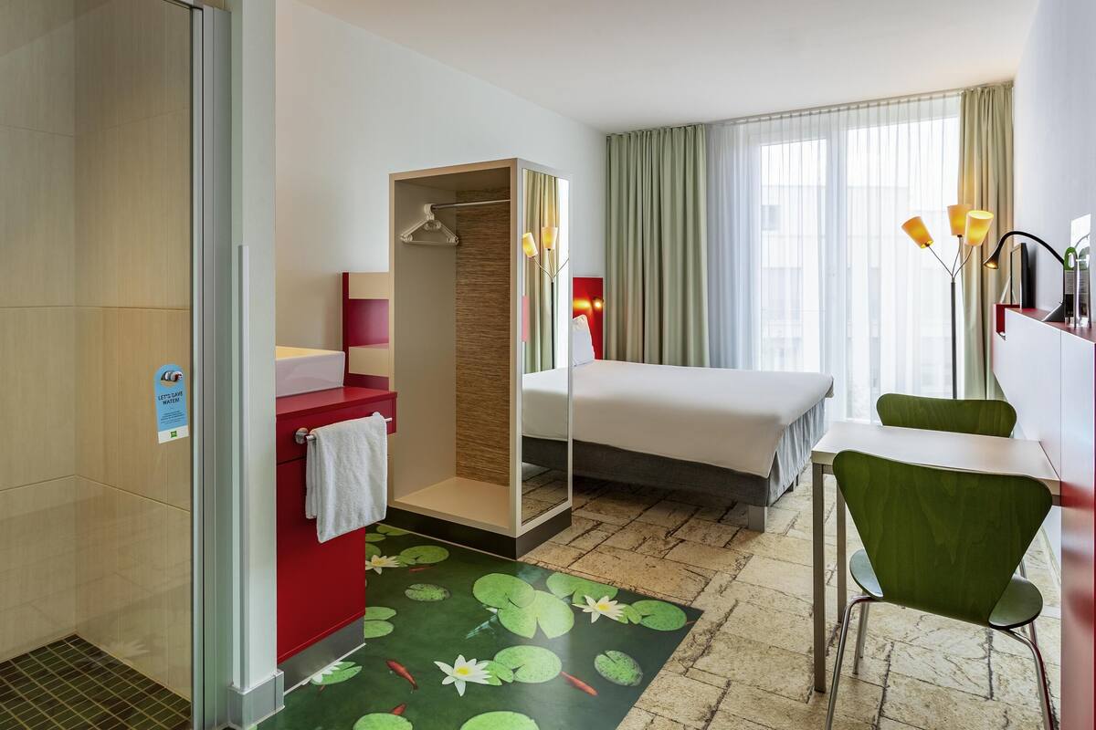 Een hotelkamer met douche, bed, bureau en stoel.