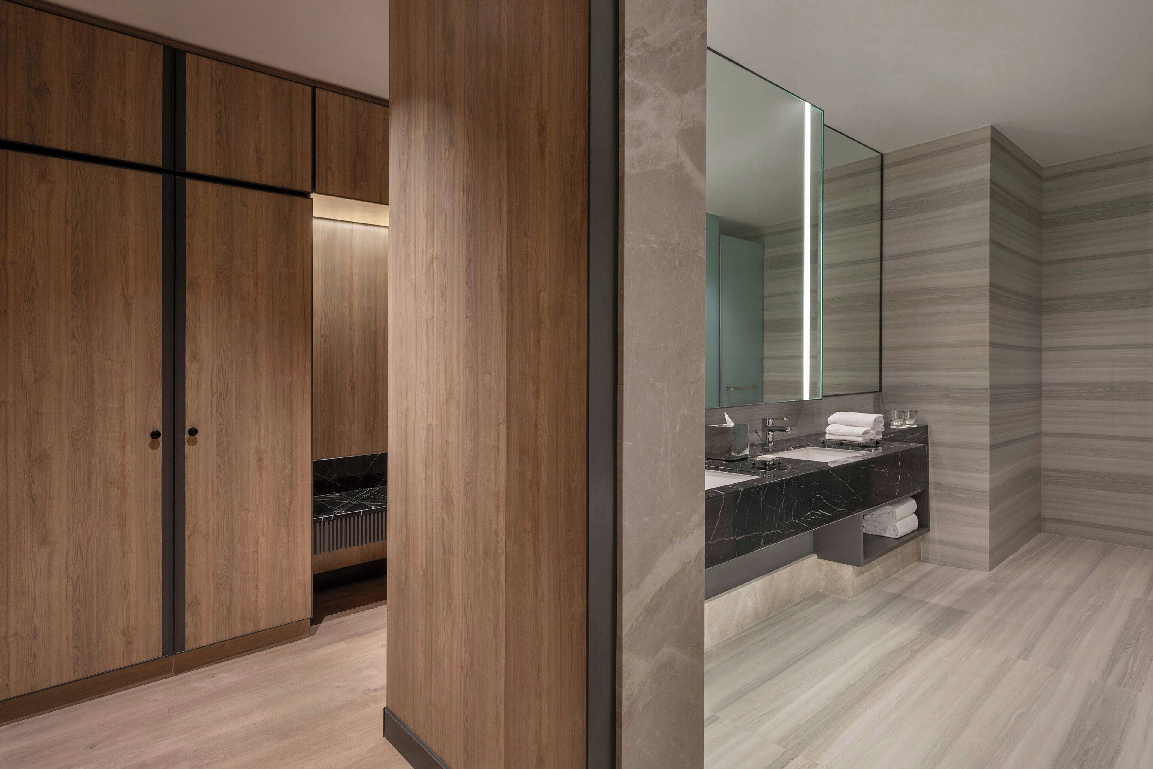 A modern bathroom with wooden cabinets, a large mirror, and a marble countertop.