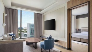 Habitación de hotel moderna con un ventanal grande, televisor de pantalla plana, sofá, mesa de centro y cama.