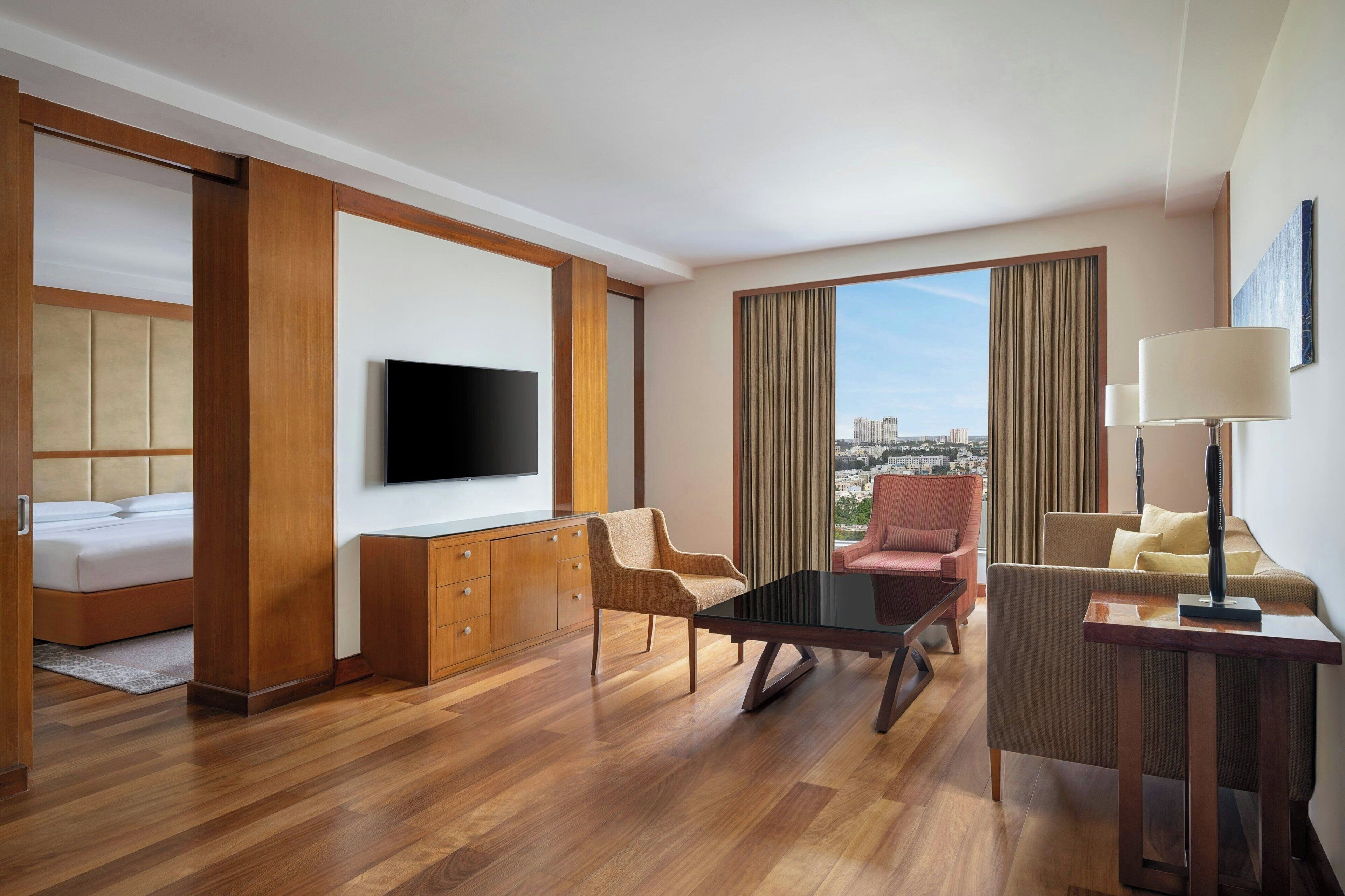 A hotel room with a bed, a TV, a desk, a chair, and a view of the city.