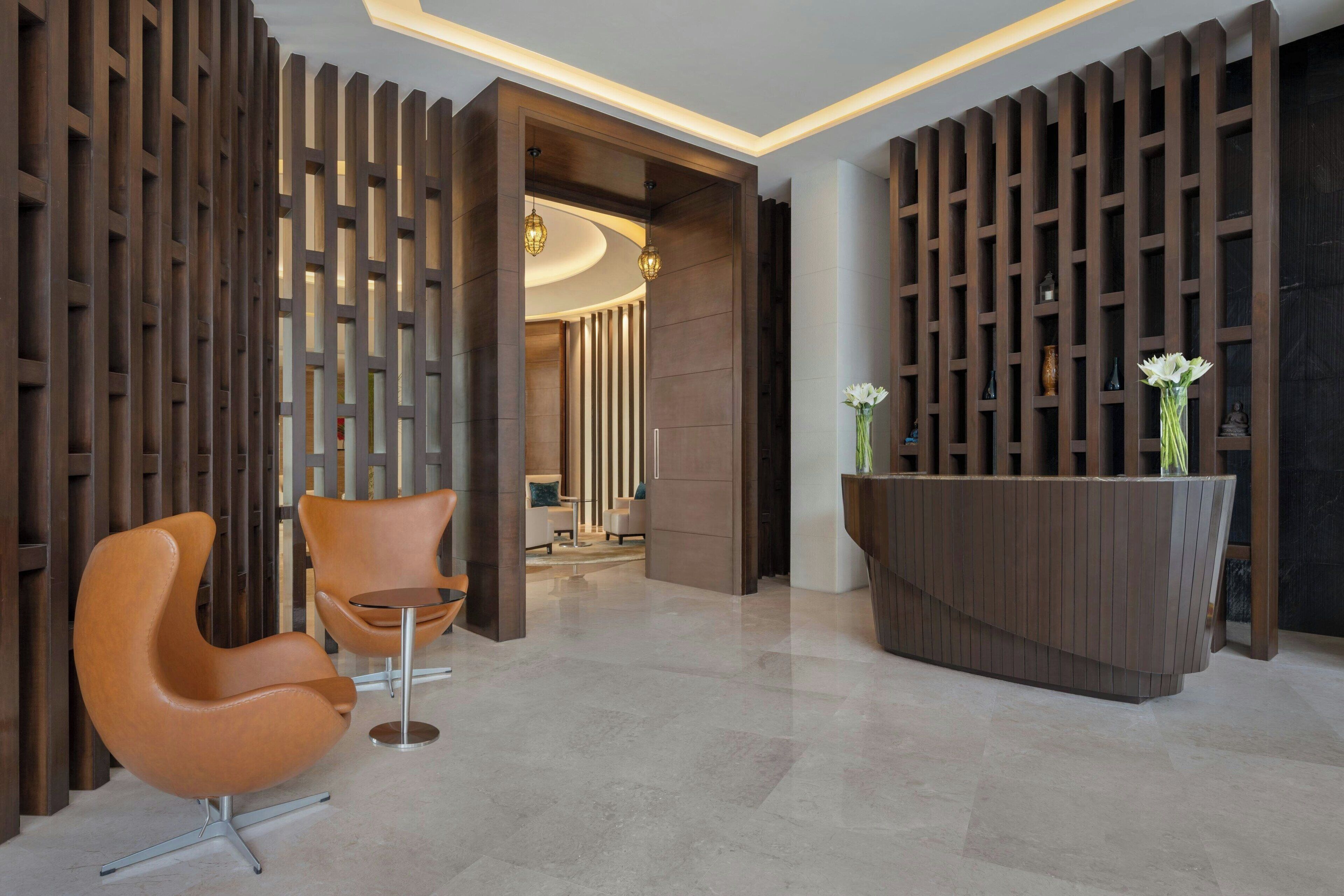 A modern reception area with a wooden reception desk, two orange chairs, and a decorative wall with vertical slats.