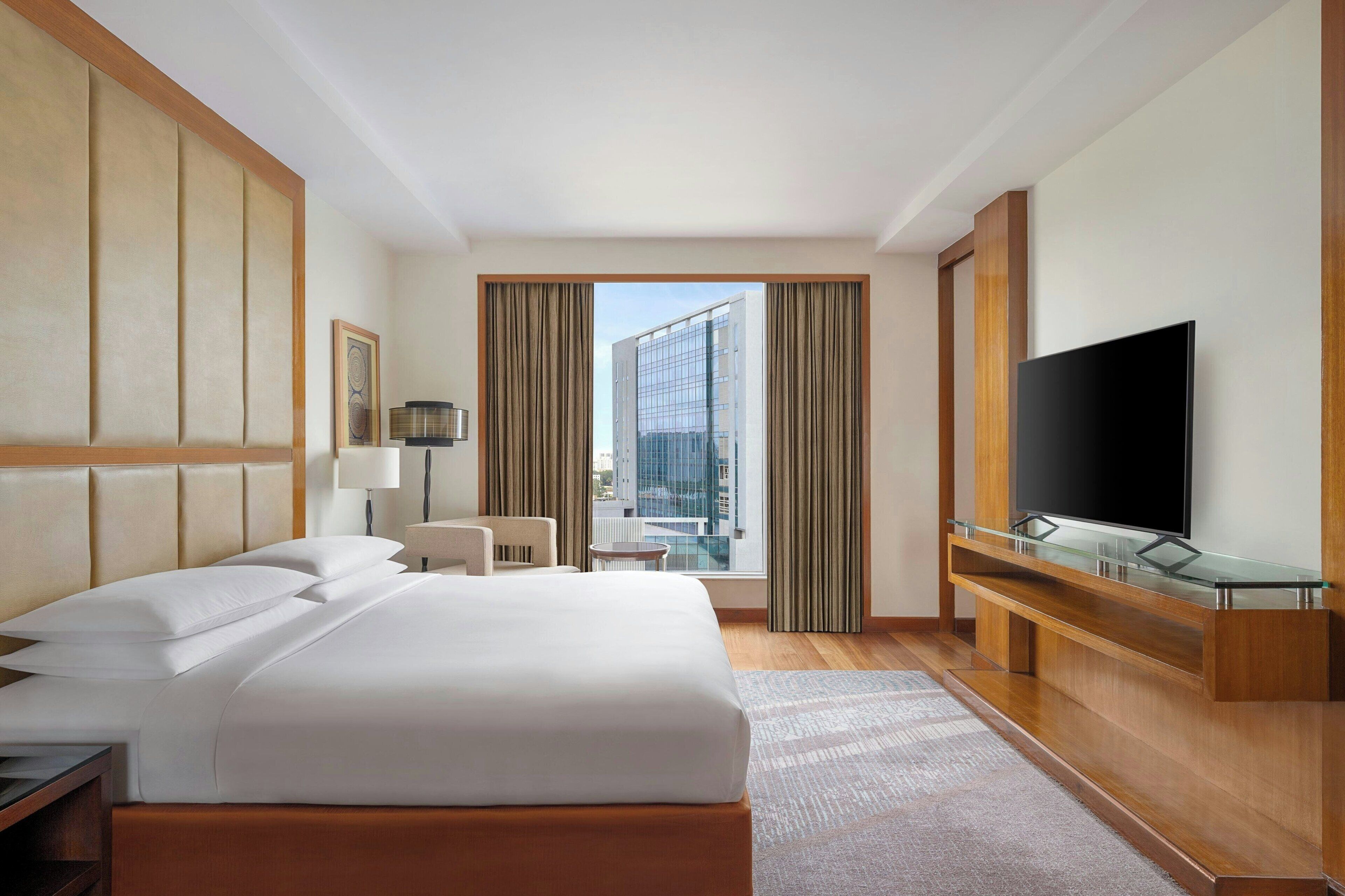 Une chambre d’hôtel avec un grand lit, une télévision, un bureau et une vue sur le paysage urbain par la fenêtre.
