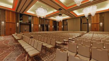 A large conference room with rows of chairs, a patterned carpet, and chandeliers.