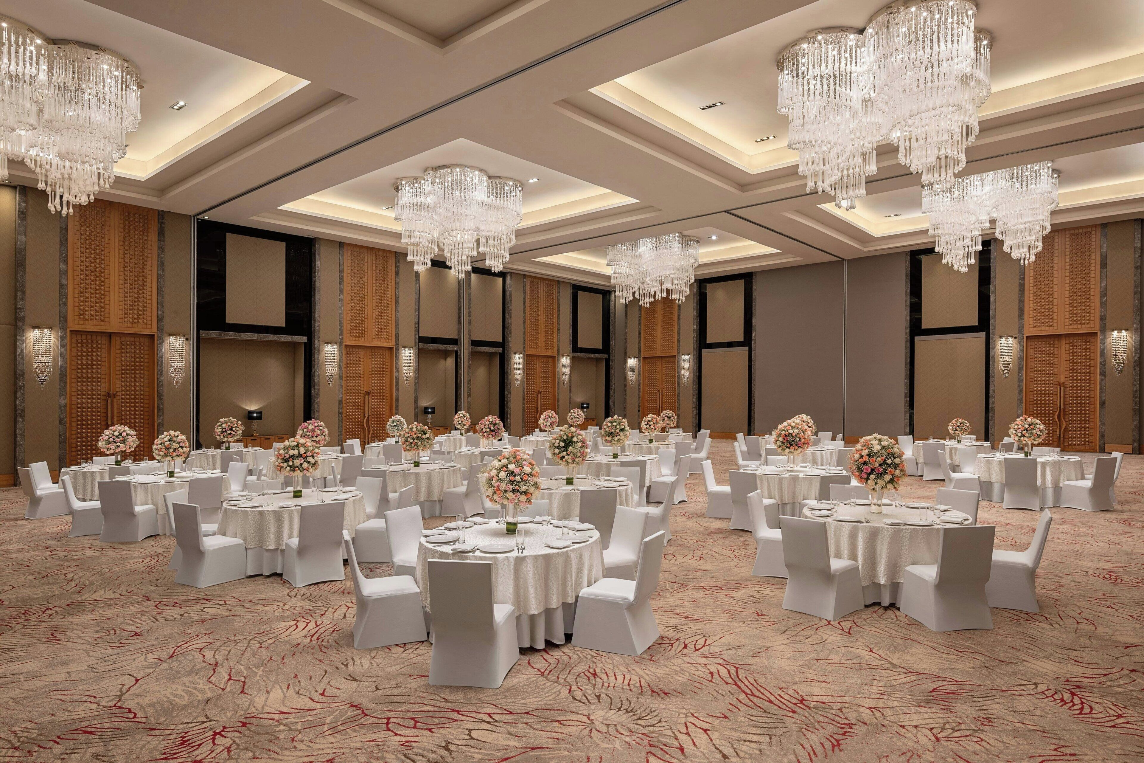 A banquet hall with round tables, white chairs, and chandeliers.