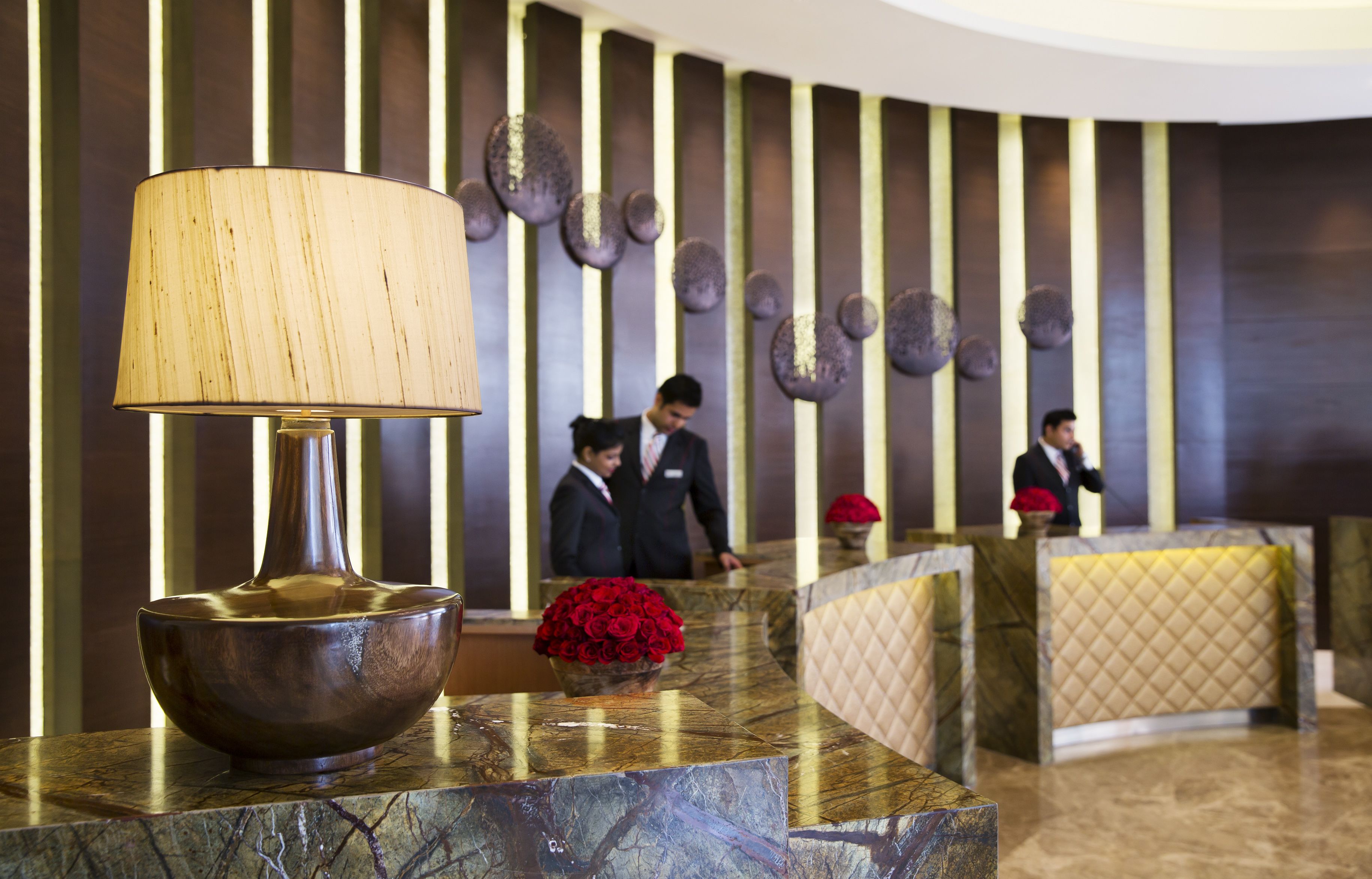 A reception area with a marble counter, a lamp, and a vase of red roses.
