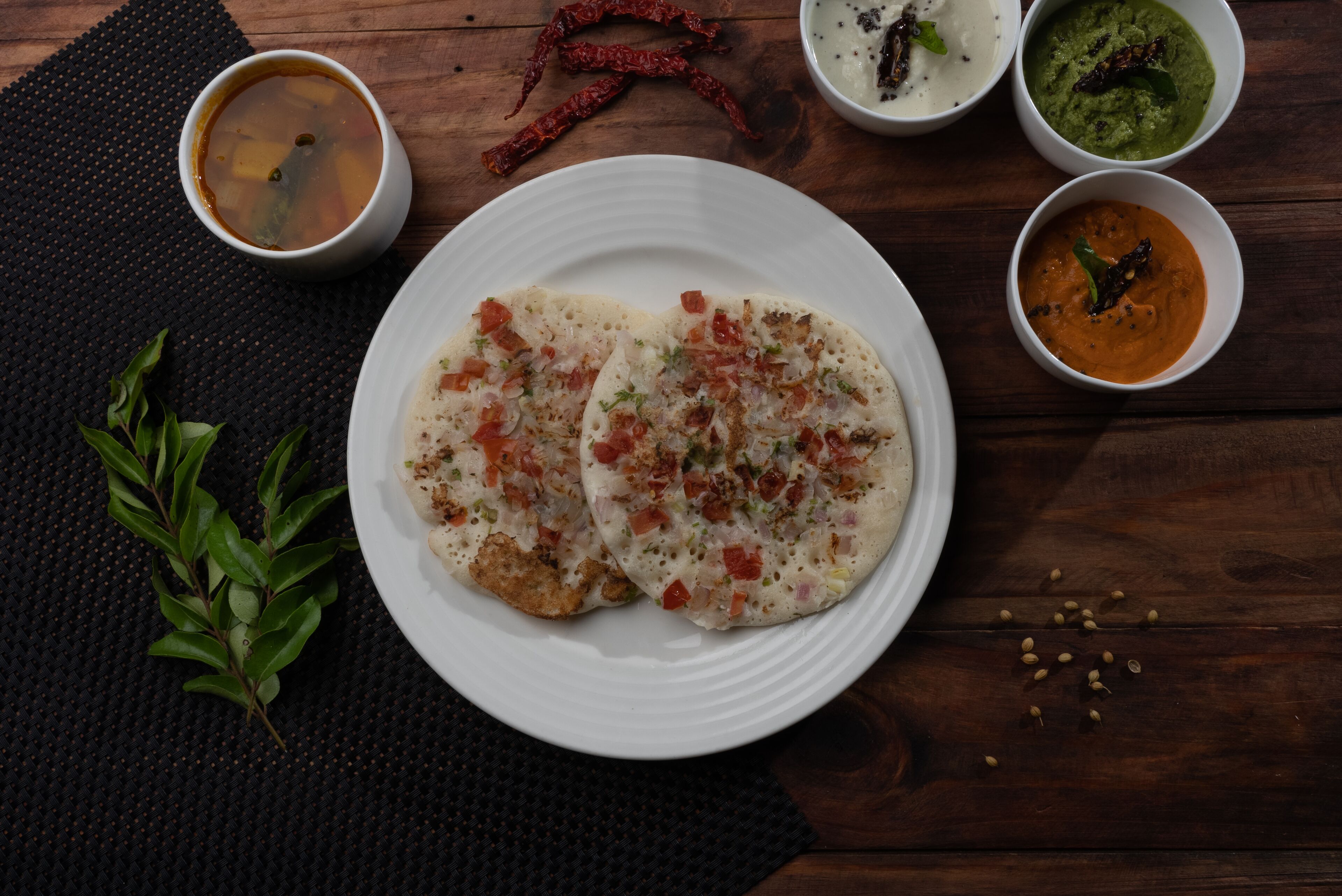 A plate of food with two pieces of flatbread topped with vegetables and a side of soup.