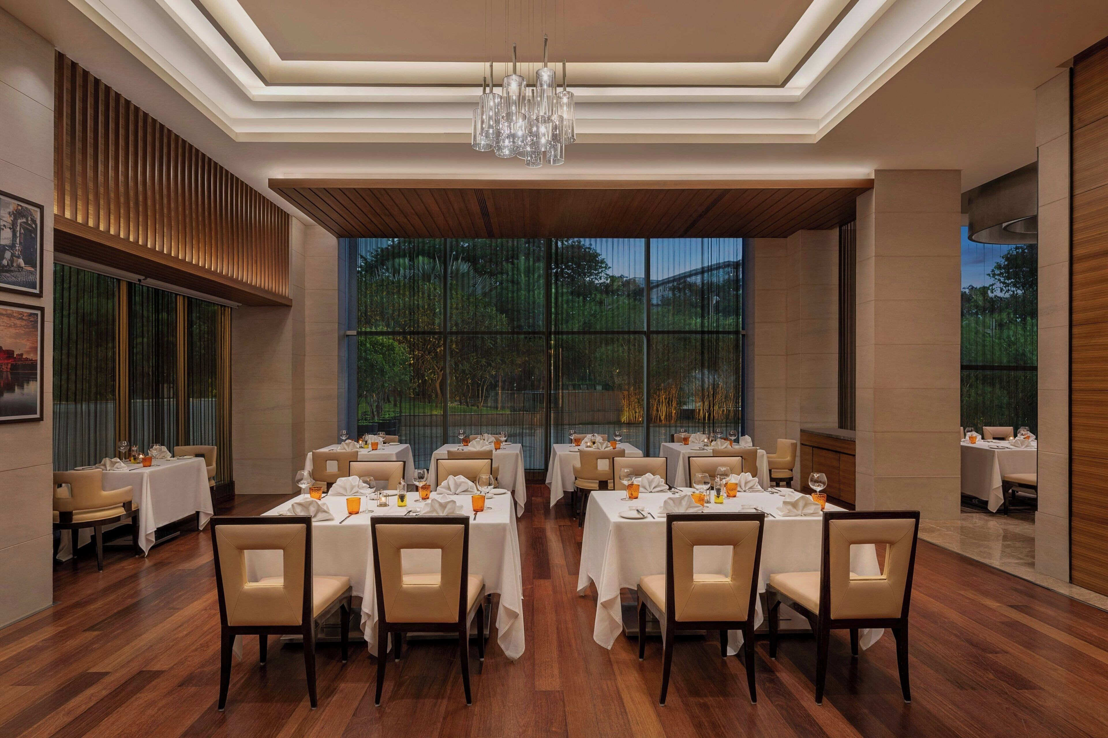 A restaurant with multiple tables and chairs, large windows, and a chandelier.