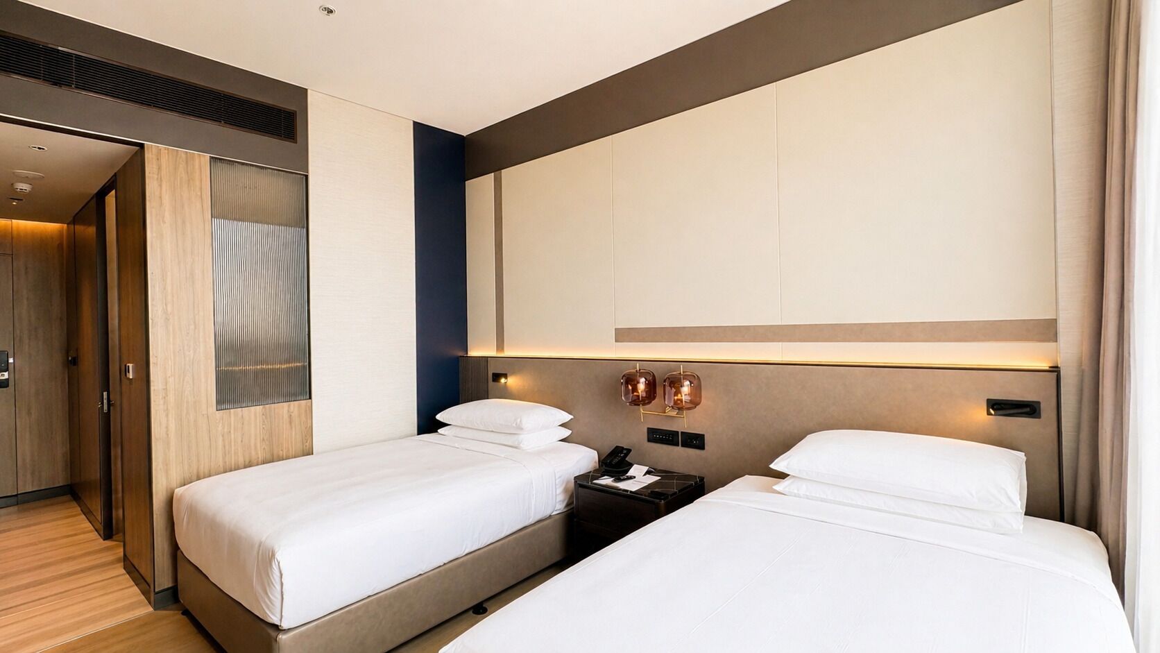 Une chambre d’hôtel avec deux lits, une armoire en bois, un grand miroir et un luminaire fixé au mur.