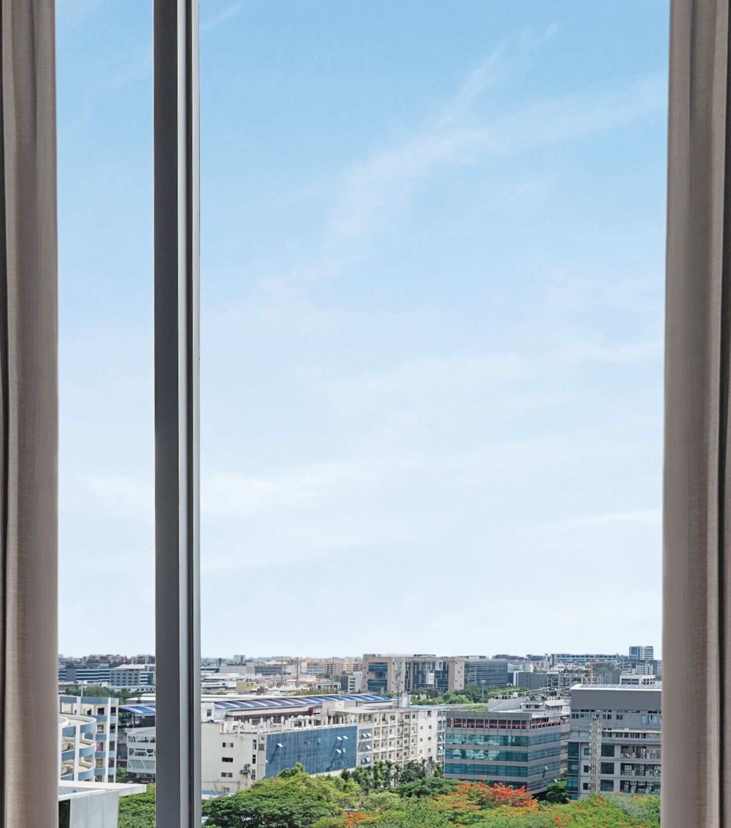 En stadsbild sedd genom ett fönster, med moderna byggnader och en klar himmel.