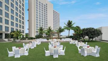 A hotel courtyard with multiple round tables set up for an event, surrounded by white chairs and palm trees.