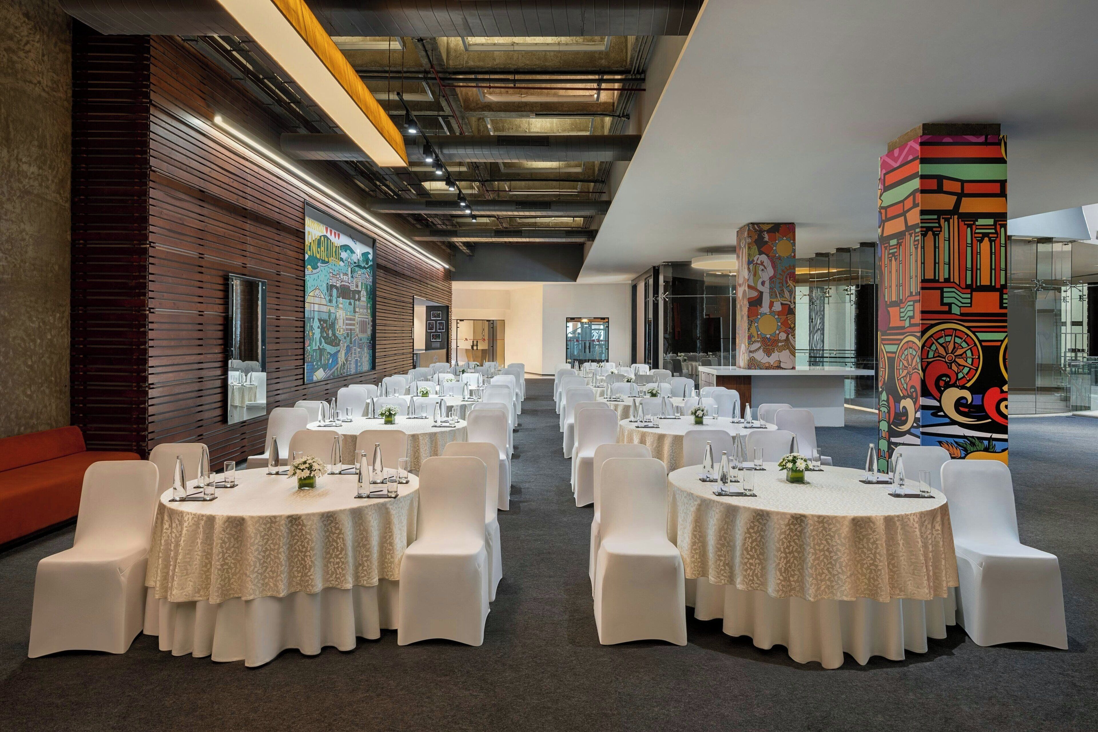 A conference room with round tables, white chairs, and a wooden wall with a mural.