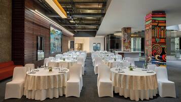 A conference room with round tables, white chairs, and a wooden wall with a mural.