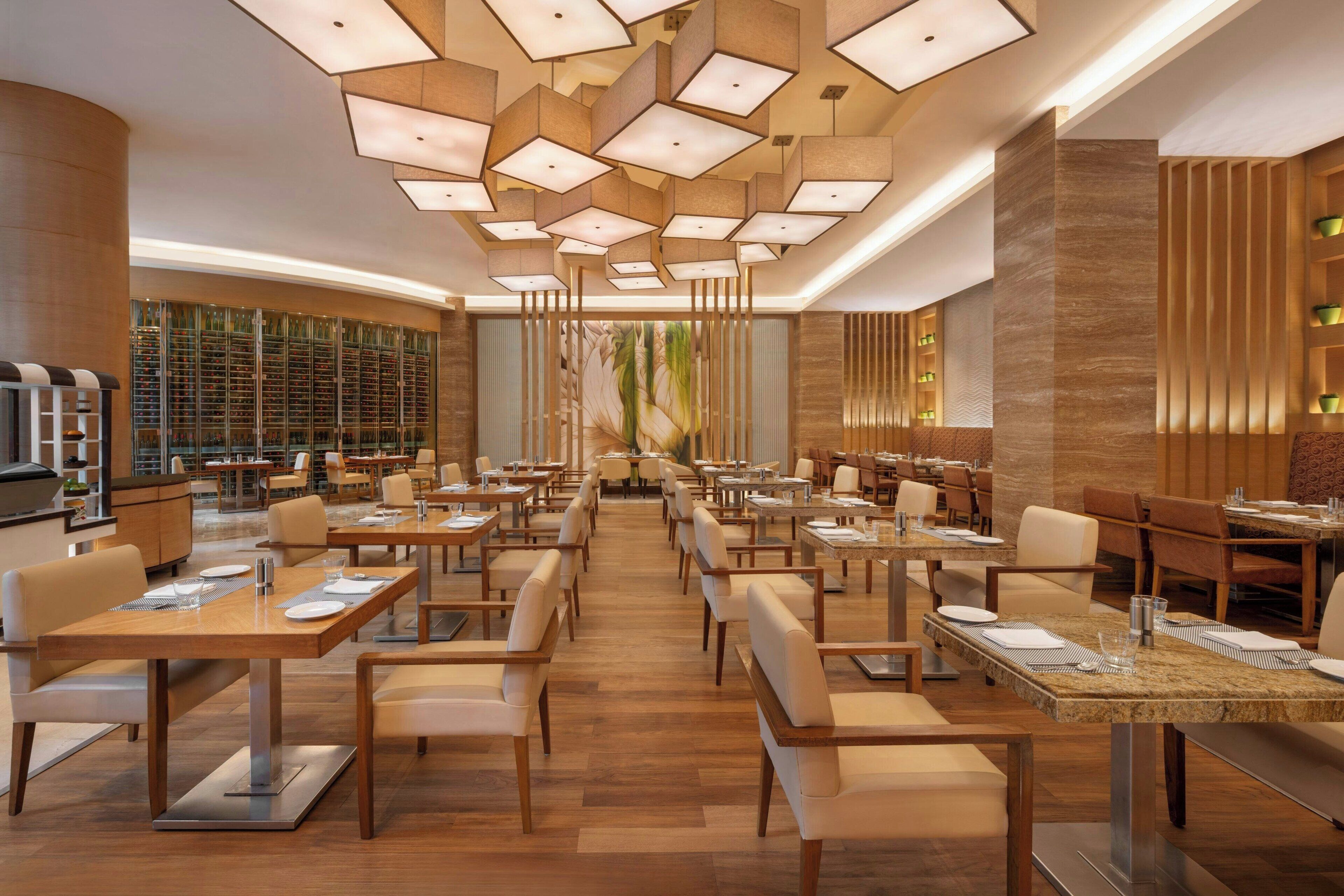 A modern restaurant with wooden tables and chairs, a central aisle, and a decorative ceiling.