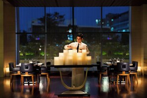 A man seated at a table with candles, surrounded by chairs and tables in a room with large windows. - Bengaluru Marriott Hotel Whitefield (Bengaluru)