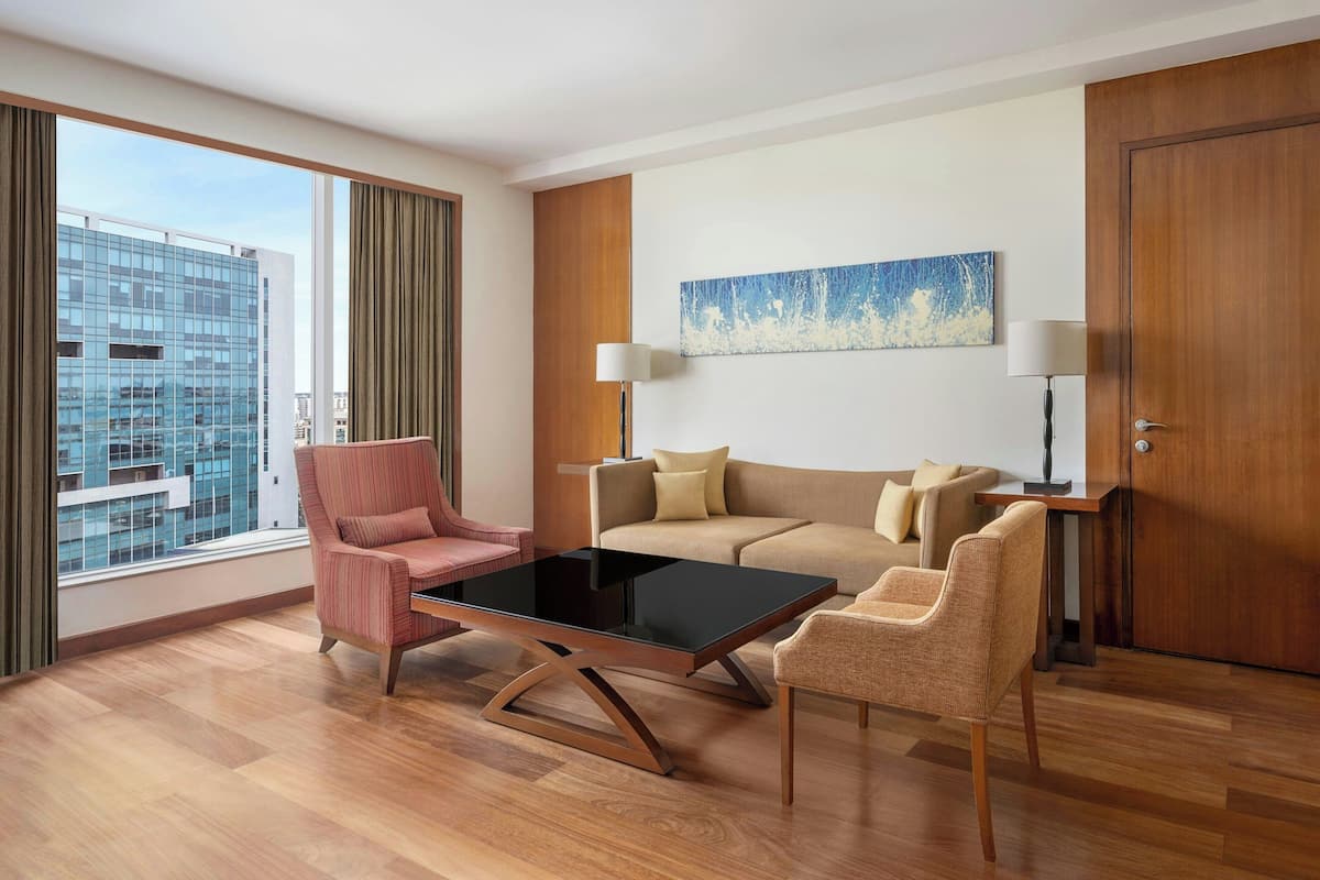A modern hotel room with a large window, a sofa set, a coffee table, and a lamp.