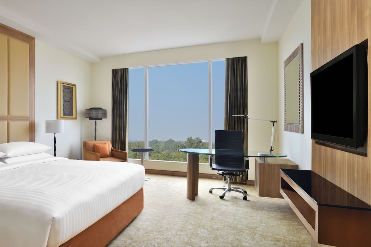 A hotel room with a bed, desk, TV, and large windows.