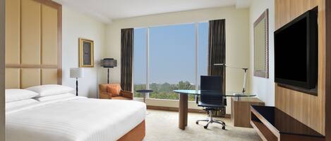 Habitación de hotel con cama, escritorio, televisión y ventanas amplias.