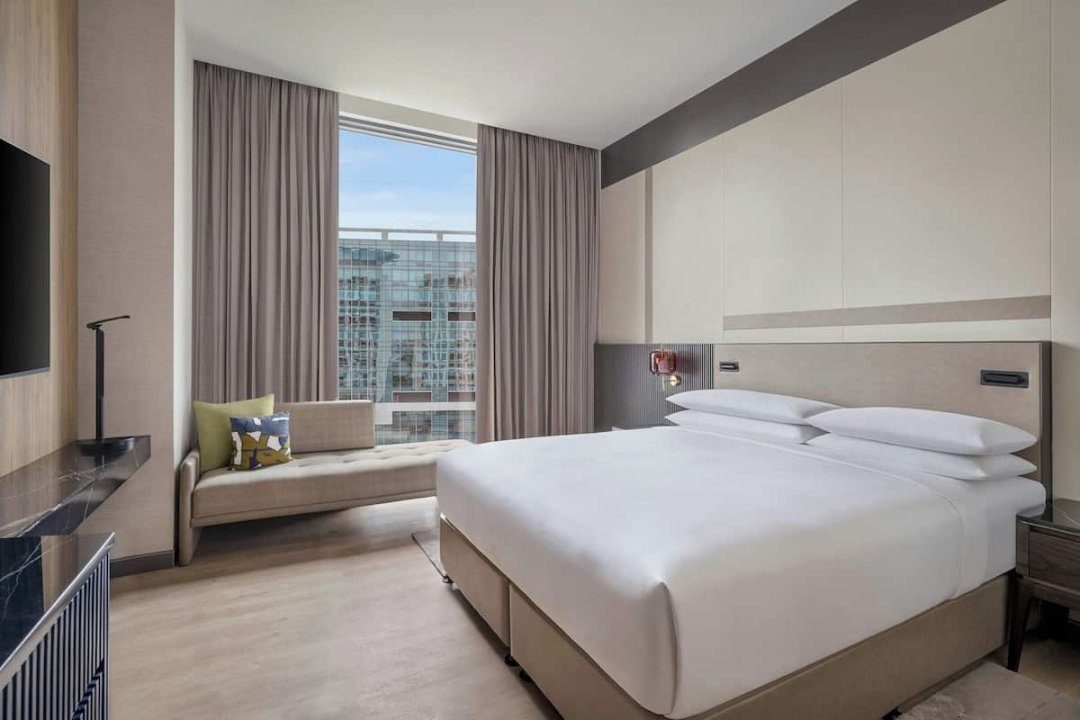 A hotel room with a large bed, a sofa, a TV, and a view of a cityscape.