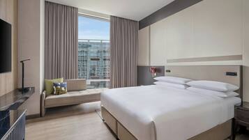 A hotel room with a large bed, a sofa, a TV, and a view of a cityscape.