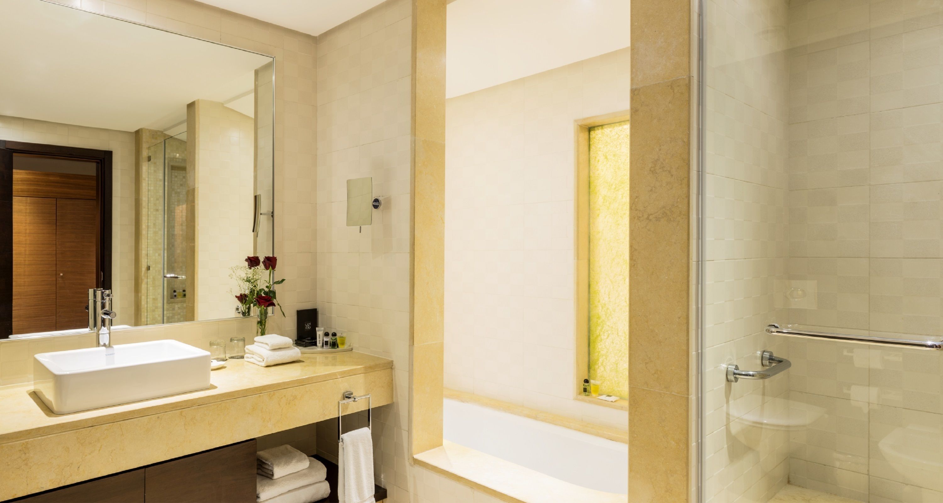 A modern bathroom with a large mirror, a sink, a glass shower enclosure, and a bathtub.