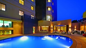 A swimming pool with a sunken seating area, surrounded by a building with multiple floors and balconies. - Corp Amman Hotel (Amman)