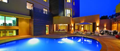 A swimming pool with a sunken seating area, surrounded by a building with multiple floors and balconies.