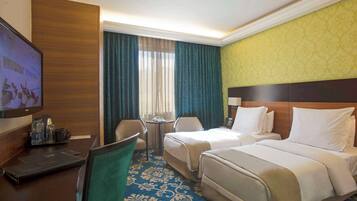 A hotel room with two beds, a desk with a laptop, a TV, and a small table with a lamp.