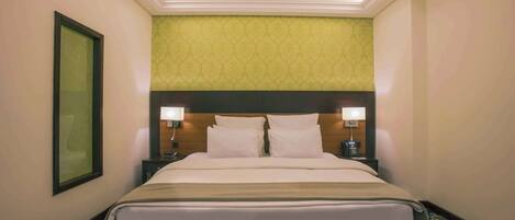 A hotel room with a large bed, two bedside tables with lamps, a headboard, a framed picture on the wall, and a patterned carpet.