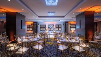 Un salón de banquetes con mesas redondas dispuestas para un evento formal, con una alfombra estampada en azul y modernos candelabros.