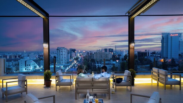 A rooftop lounge with a city view, seating, and a table with drinks. - Corp Amman Hotel (Amman)