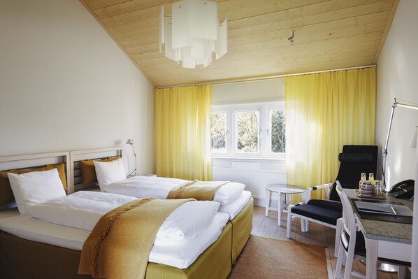 Habitación de hotel con dos camas, un escritorio, una silla, una lámpara y una ventana con cortinas.