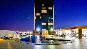Un área de piscina en la azotea con sillones reclinables y vistas a un edificio alto por la noche.