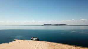 Escena costera con una playa arenosa, mar tranquilo y un barco amarrado cerca de la orilla.