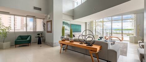 A spacious living area with a high ceiling, large windows, and a view of the outdoors.