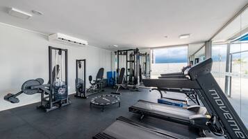 A modern gym with various exercise equipment, including treadmills and weight machines, and large windows offering a view of the outdoors.