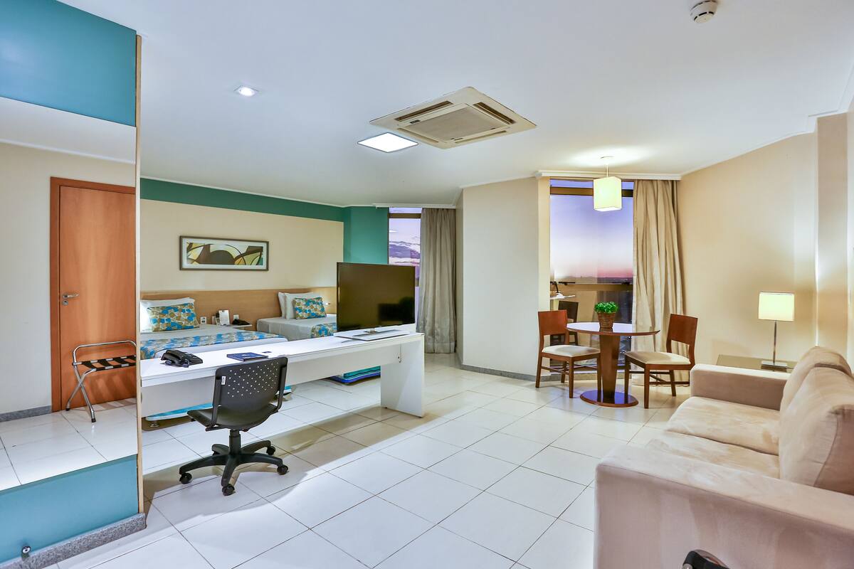 Quarto de hotel com cama, escrivaninha, cadeira de escritório e sofá.
