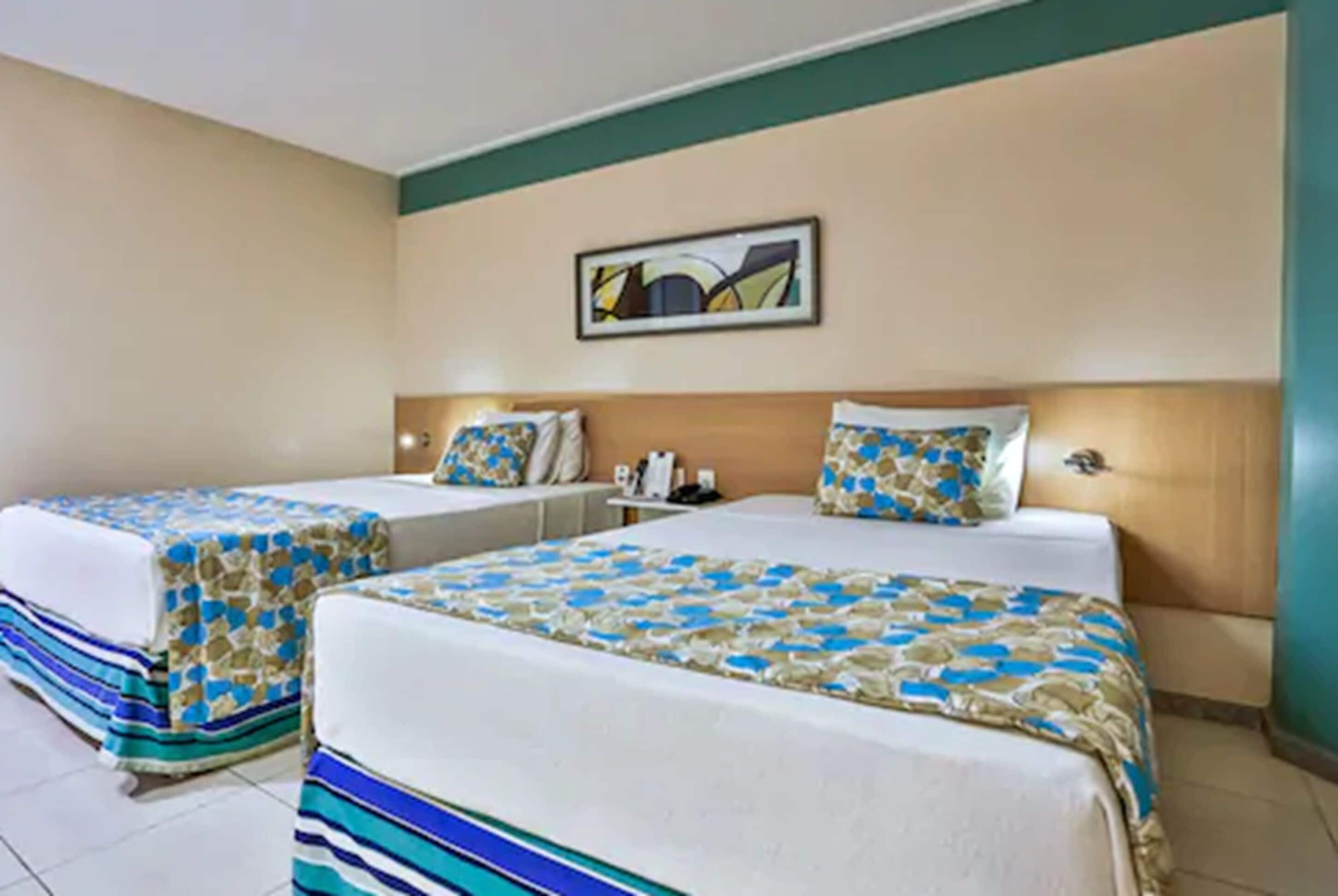 Habitación de hotel con dos camas, cada una con ropa de cama y almohadas estampadas. Un cuadro cuelga en la pared sobre las camas.