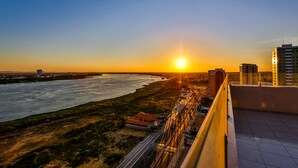 Vista del atardecer desde un edificio alto con vistas a un río y una carretera, con edificios y vegetación en primer plano.