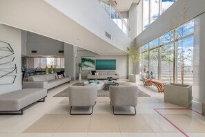 Un vaste espace de vie comprenant un canapé moderne, une table basse et deux fauteuils. Une grande fenêtre offre une vue sur l’extérieur.