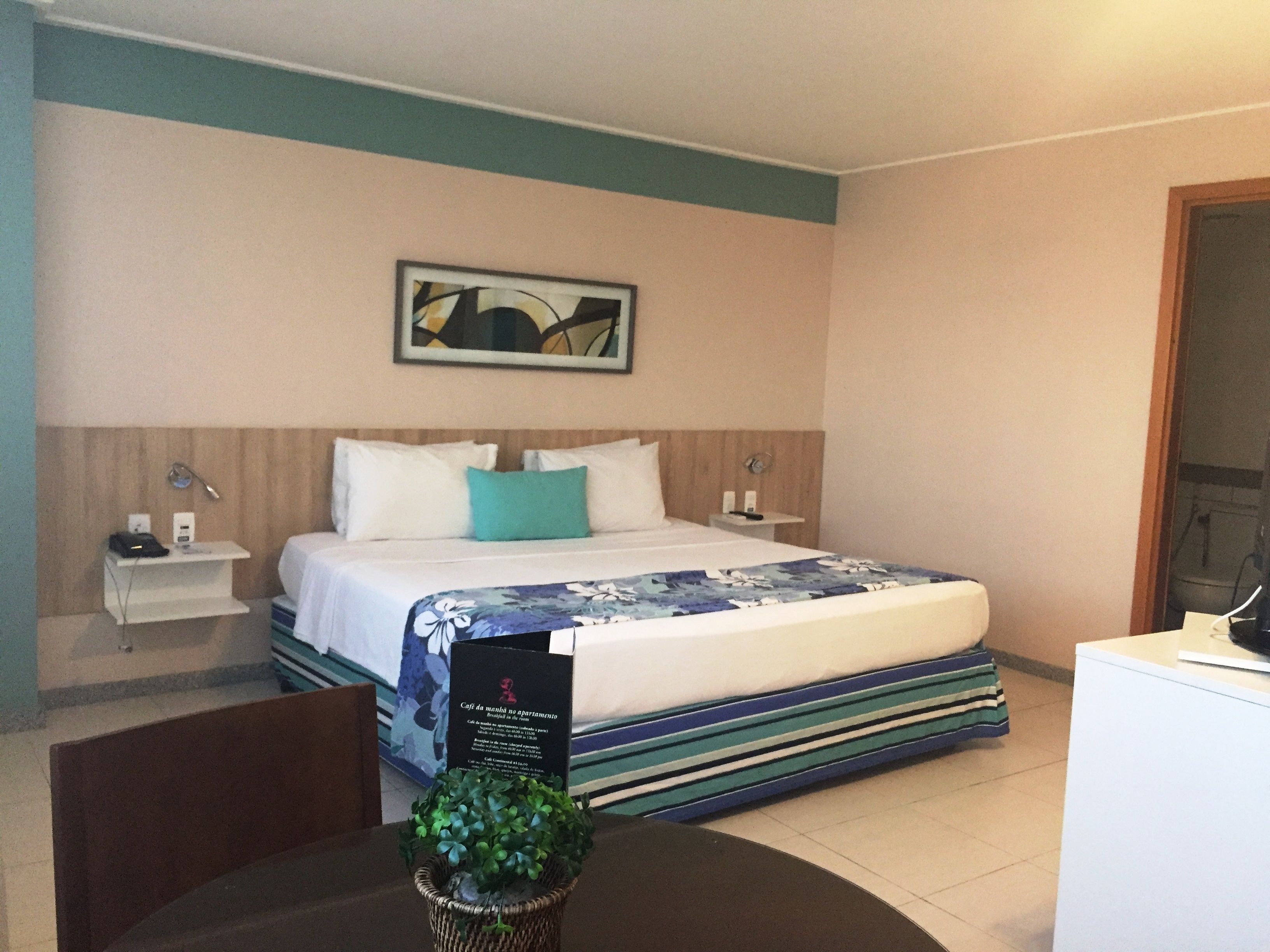 Ein Hotelzimmer mit Bett, Nachttisch, Schreibtisch und einem an der Wand hängenden Kunstwerk.