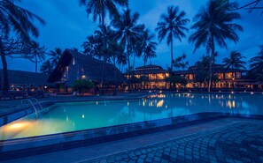 Relax by the resort's large pool surrounded by palm trees and a starry night sky.