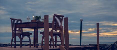 A wooden table with chairs set outdoors, overlooking a body of water under a cloudy sky.