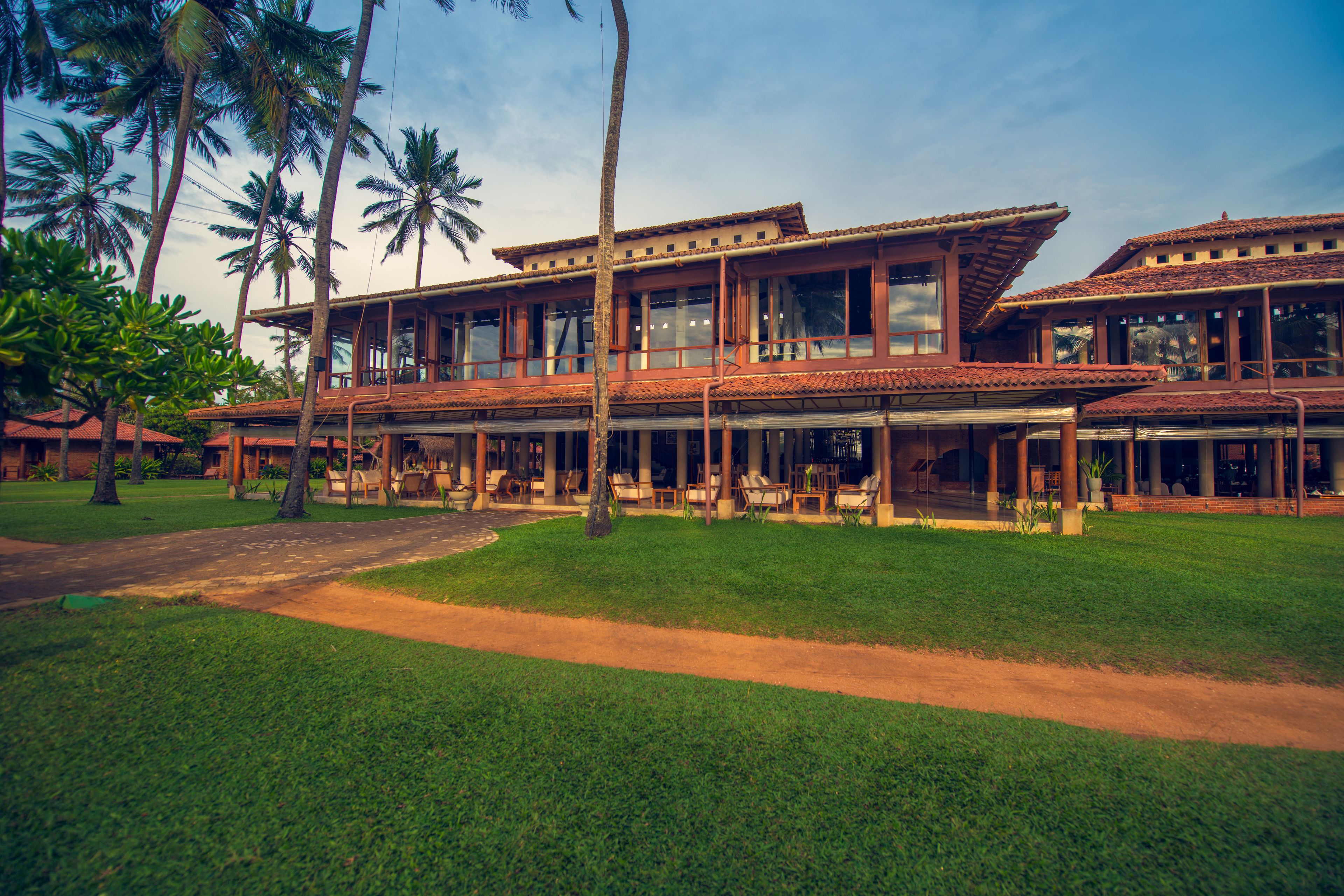 A large, two-story building with a tiled roof and large windows, surrounded by palm trees and a well-maintained lawn.