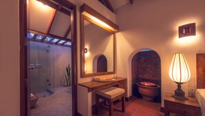 A bathroom with a wooden vanity, a large mirror, a lit lamp, and a brick wall.
