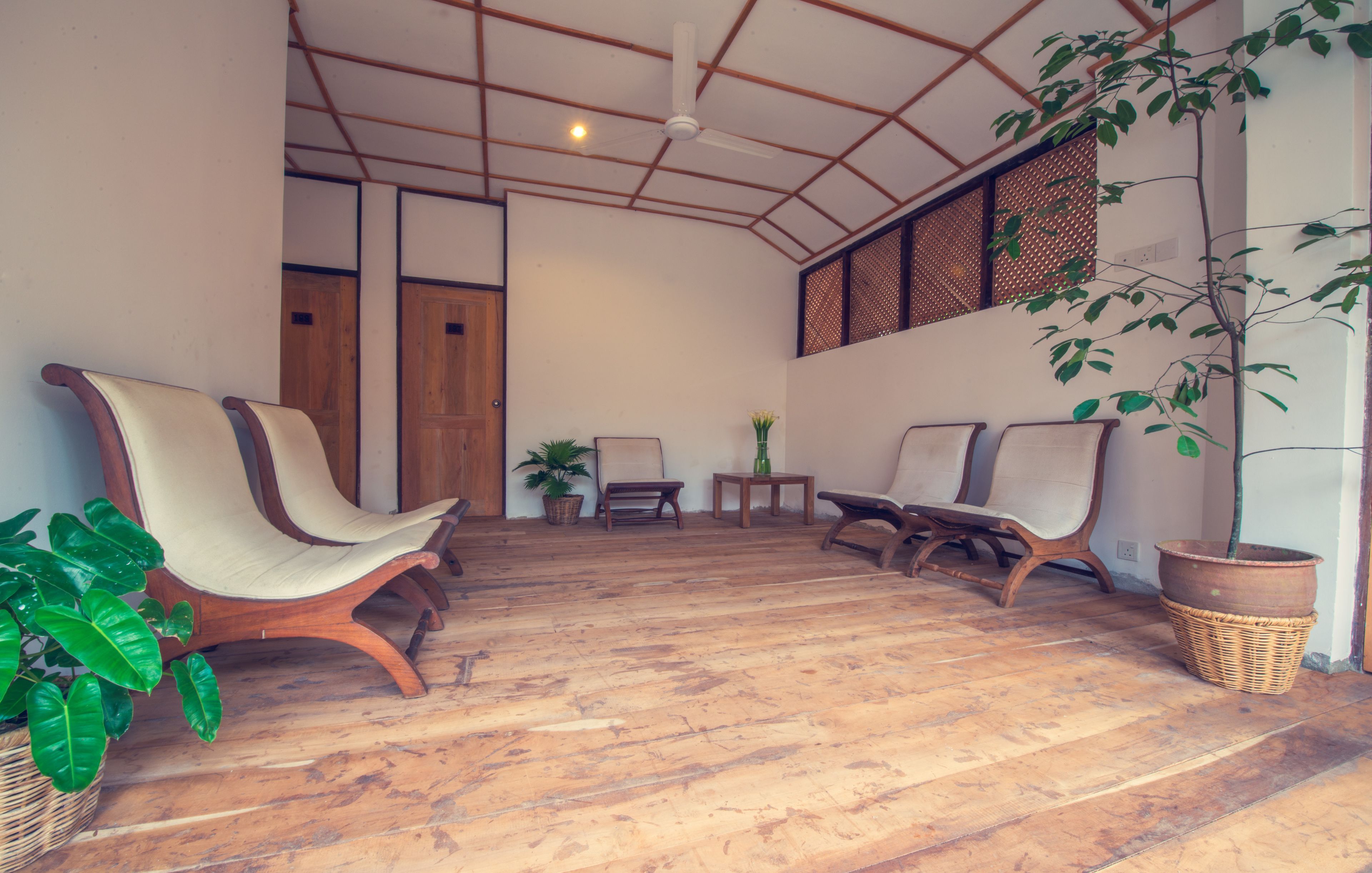 A spacious room with wooden flooring, a ceiling fan, and several wooden chairs and tables.