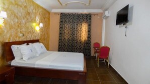 Ein Hotelzimmer mit Bett, Wandfernseher, Stuhl und kleinem Tisch.
